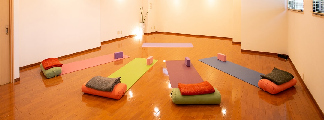 白い壁、木のフローリングにマットが敷かれたヨガスタジオ